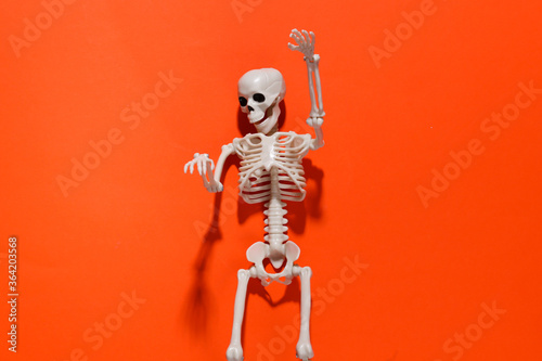 Skeleton on orange bright background. Halloween decoration, scary theme. Flat lay