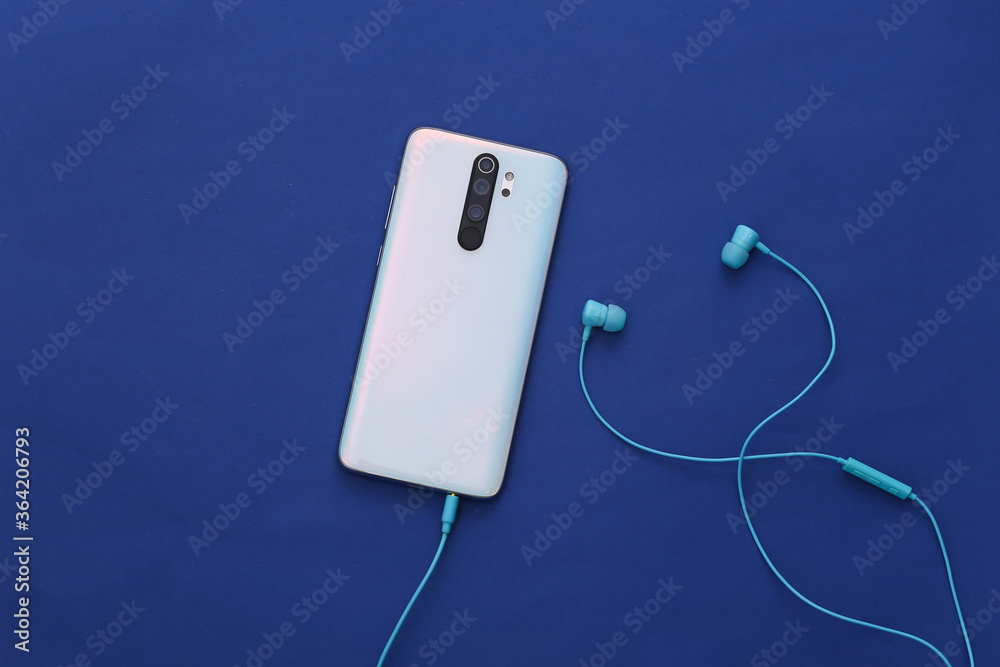 Smartphone and earphones on classic blue background. Smartphone and earphones on classic blue background.