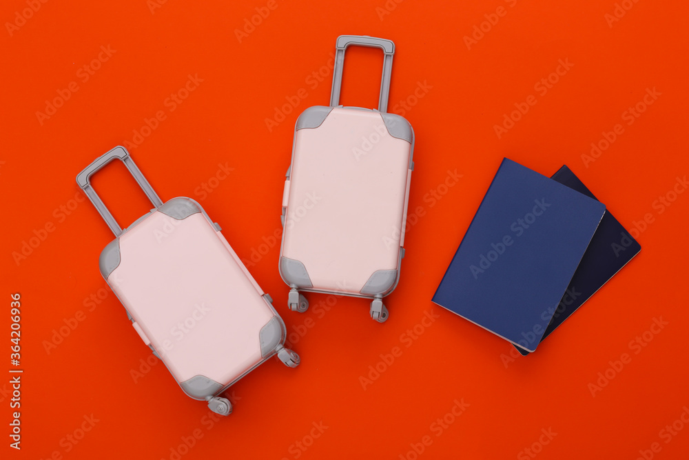 Two toy travel luggage and passport on orange background. Travel planning. Top view. Flat lay Two toy travel luggage and passport on orange background. Travel planning. Top view. Flat lay