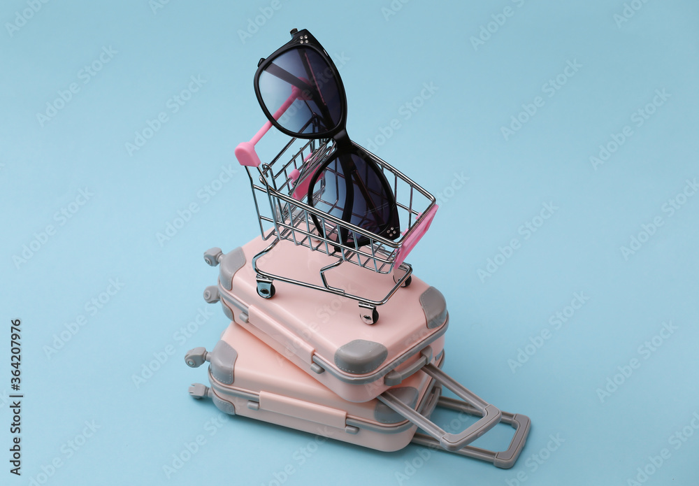 Travel, vacation or tourism concept. Two mini travel luggage suitcase and shopping trolley with sunglasses on a blue background