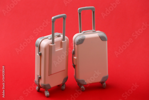 Two mini travel luggage suitcase on red background. Travel still life, vacation or tourism concept.