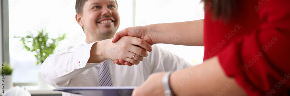 Obraz premium Close-up view of co-workers shaking hands and smiling to each other. Man in disabled carriage. Working process at company office. Employee holding folder with papers. Business concept