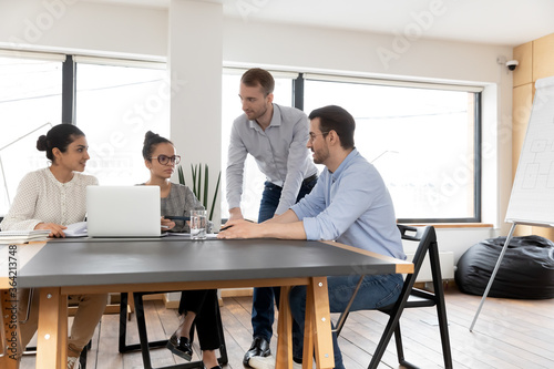 Multiracial businesspeople sit at desk in boardroom brainstorm discuss business ideas using laptop in office, diverse employees cooperate at meeting, work on computer, teamwork, collaboration concept