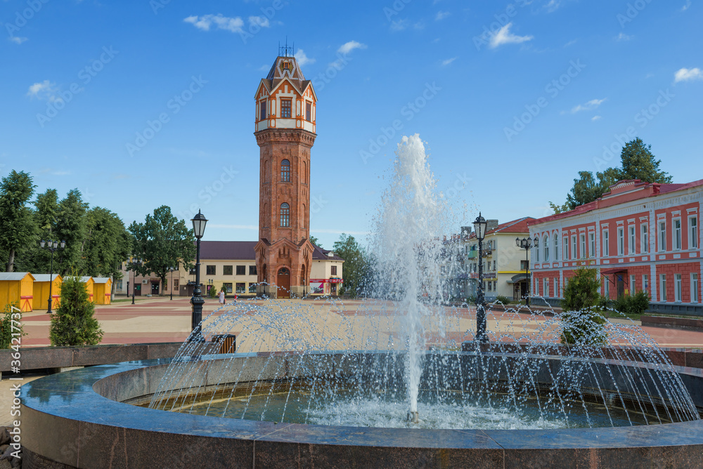 Fototapeta premium City fountain against the background of an old water tower on a sunny July morning. Staraya Russa, Russia
