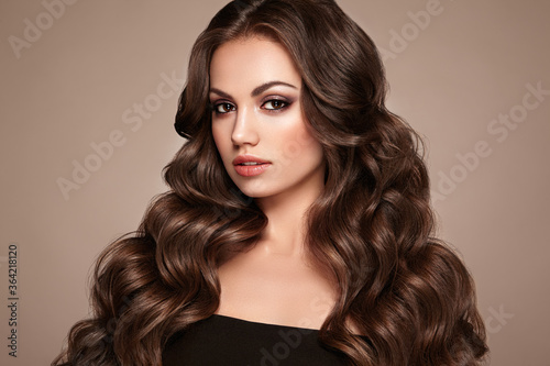 Brunette Girl with Long Healthy and Shiny Curly Hair. Care and Beauty. Beautiful Model Woman with Wavy Hairstyle. Make-Up and Black Dress