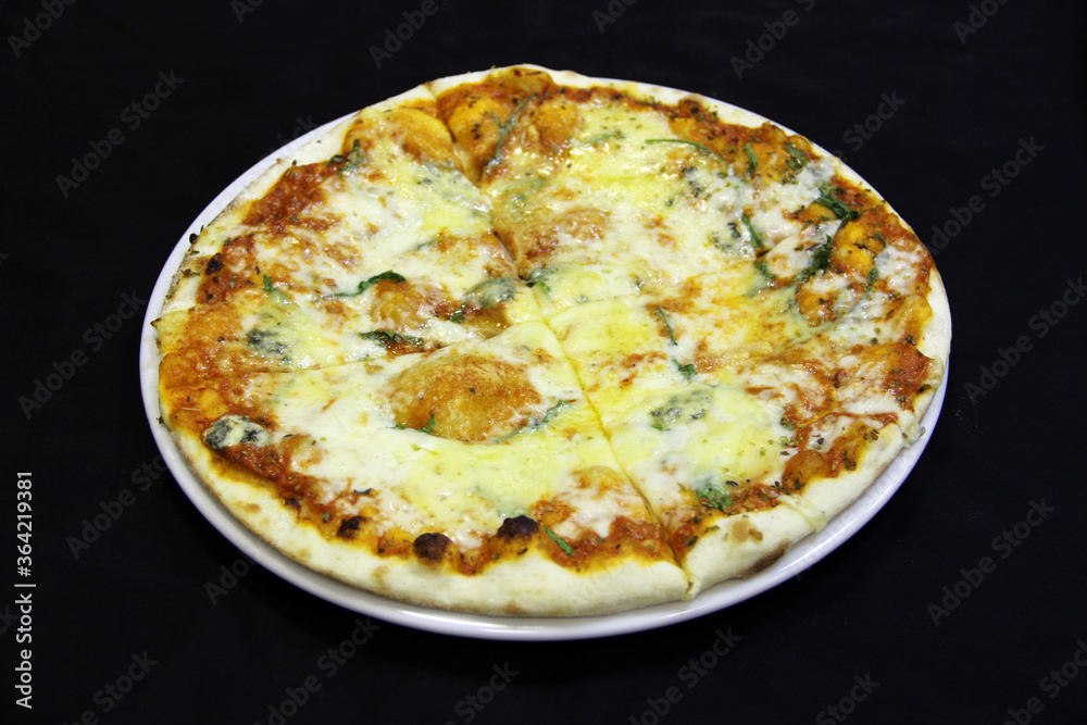 Pizza with four pieces of cheese and basil leaves on a white plate Pizza with four pieces of cheese and basil leaves on a white plate