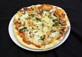 Meat pizza with cheese, mushrooms and dill on a white plate