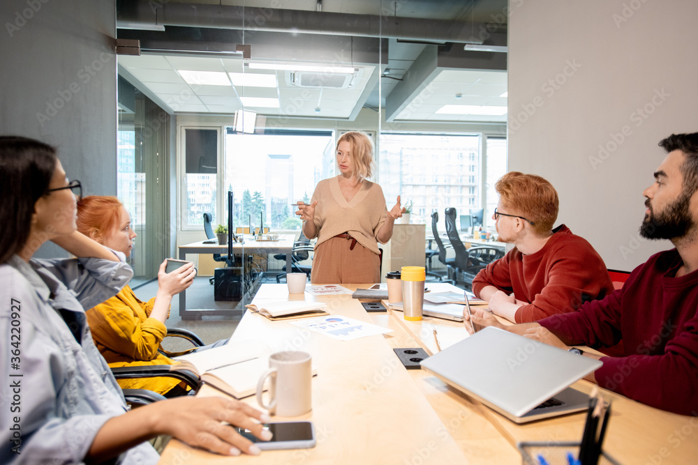 Obraz premium Mature woman standing by table in front of her young intercultural colleagues