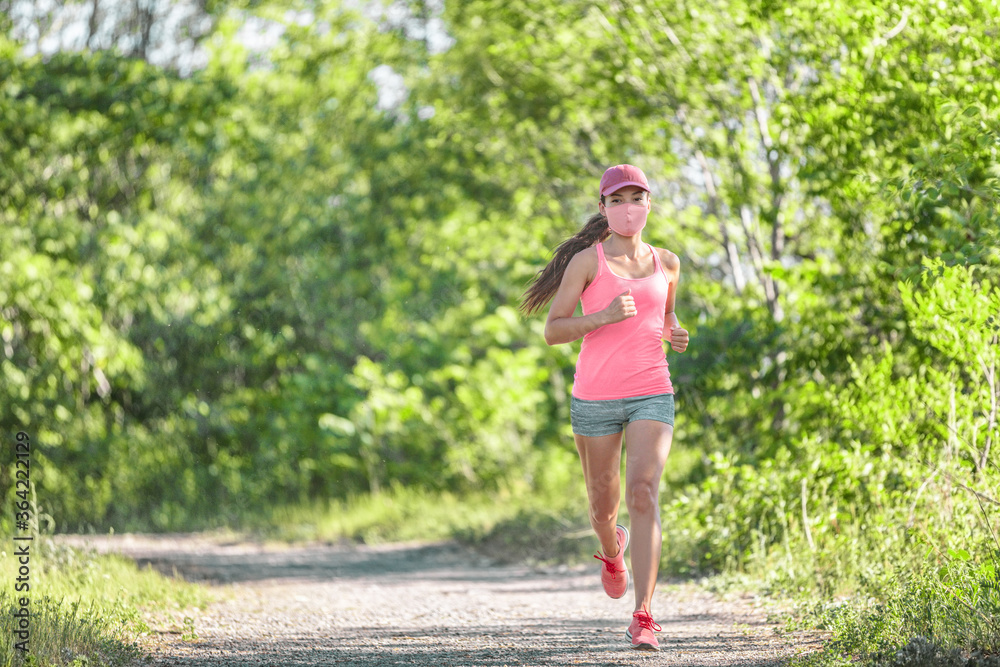 COVID-19 running woman wearing mask while exercising cardio outdoor on run workout in summer park nature. Sport lifestyle.