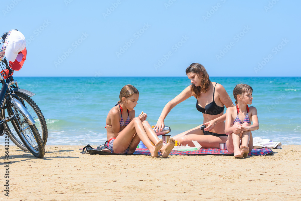 Children watch mom pouring mugs of tea on the seashore on a warm summer day Children watch mom pouring mugs of tea on the seashore on a warm summer day