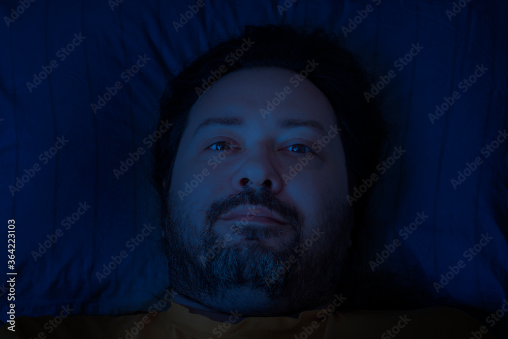 A middle-aged bearded man lies on a pillow late at night with a half smile on his face. Concept - insomnia and pleasant thoughts.