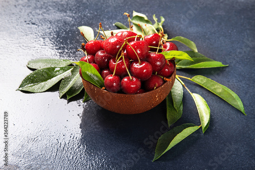 Plate with fresh cherries with green leaves. Black background.