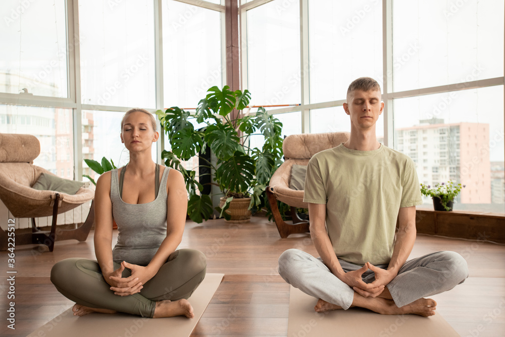 Young serene couple in sportswear crossing their legs during meditation practice Young serene couple in sportswear crossing their legs during meditation practice