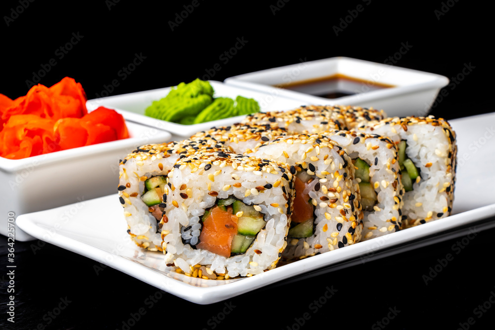 Rolls with salmon, cucumber and sesame seeds on a white plate on a dark background. Sushi menu. Japanese food. Rolls with salmon, cucumber and sesame seeds on a white plate on a dark background. Sushi menu. Japanese food.