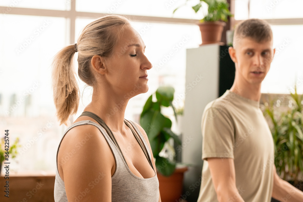Young serene blond woman in sportswear meditating in pose of lotus with trainer Young serene blond woman in sportswear meditating in pose of lotus with trainer