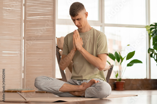 Serene and concentrated young man keeping his hands put together by bent head