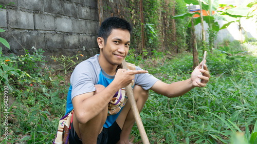 Asian man is gardening and thinking while looking at his cellphone photo