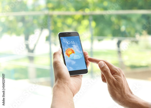 Man using weather forecast app on smartphone near window, closeup