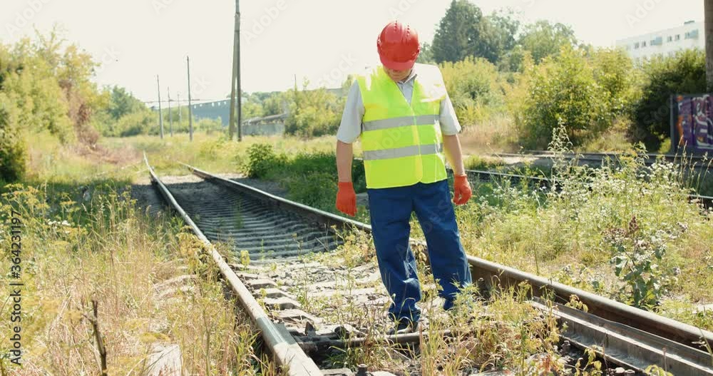 Senior engineer in uniform and helmet checks the railway in sunny day Senior engineer in uniform and helmet checks the railway in sunny day