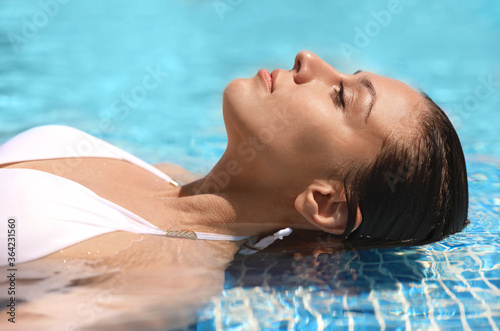 Beautiful young woman relaxing in outdoor swimming pool