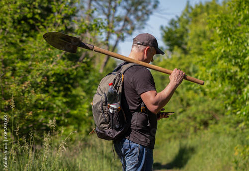 A man with a shovel and a backpack is walking through the forest. Harvesting wild plants. Nature, Environment And Ecology. 