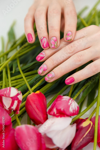 Female hands with spring manicure and tulips nail art, floral design on flowers background. Beauty, fingernails and hands care concept. Vertical shot.