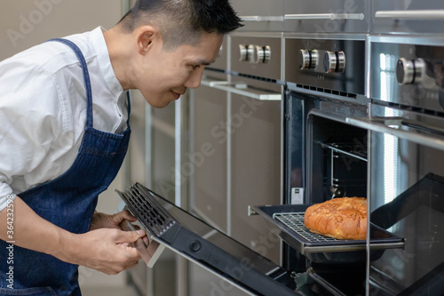 Asian baker smile and looking at the fresh baked bread from the oven in the kitchen. Man cooking  and bakery concept.
