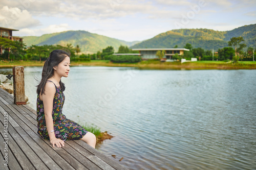 Asian girl sitting on wooden bridge in garden at evening