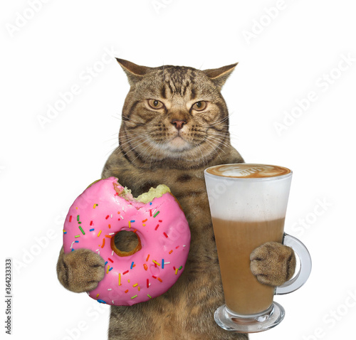 The beige cat is holding a pink bitten donut and a glass of cappuccino. White background. Isolated.