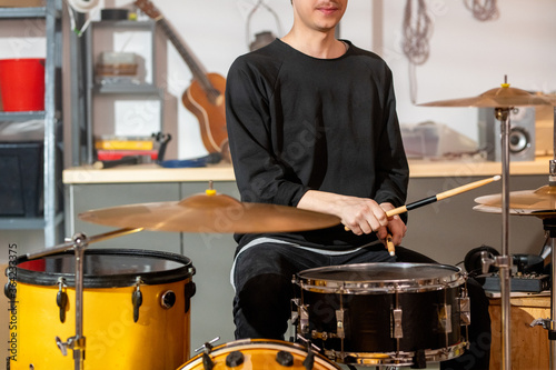 Young musician in casualwear beating one of drums with wooden drumsticks photo