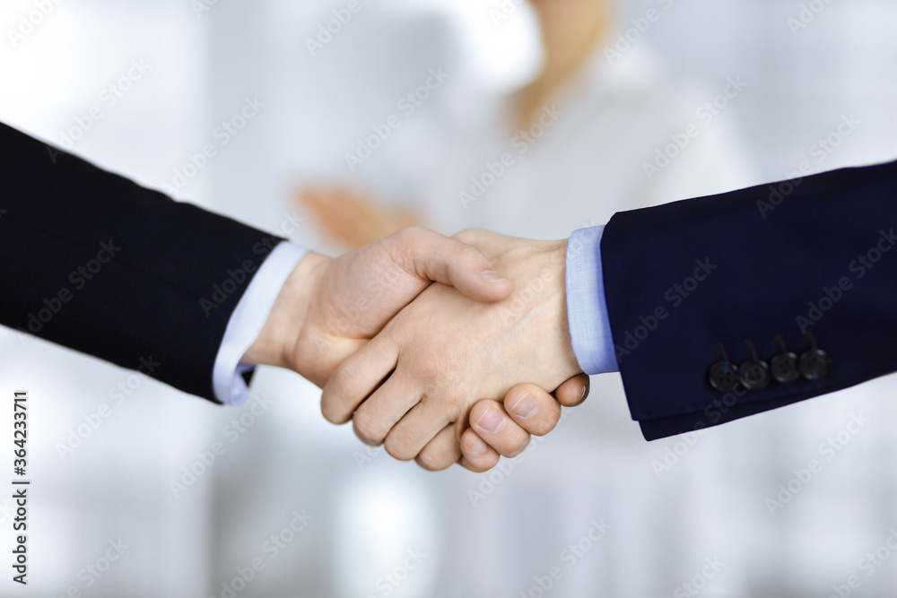 Business people shaking hands at meeting or negotiation, close-up. Group of unknown businessmen and a woman standing in a modern office. Teamwork, partnership and handshake concept