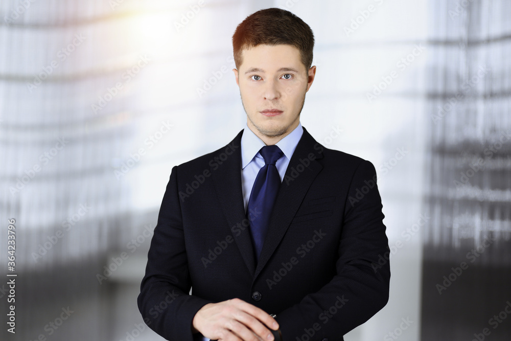 Young businessman in a suit, while standing in a sunny office. Business success concept nowadays Young businessman in a suit, while standing in a sunny office. Business success concept nowadays