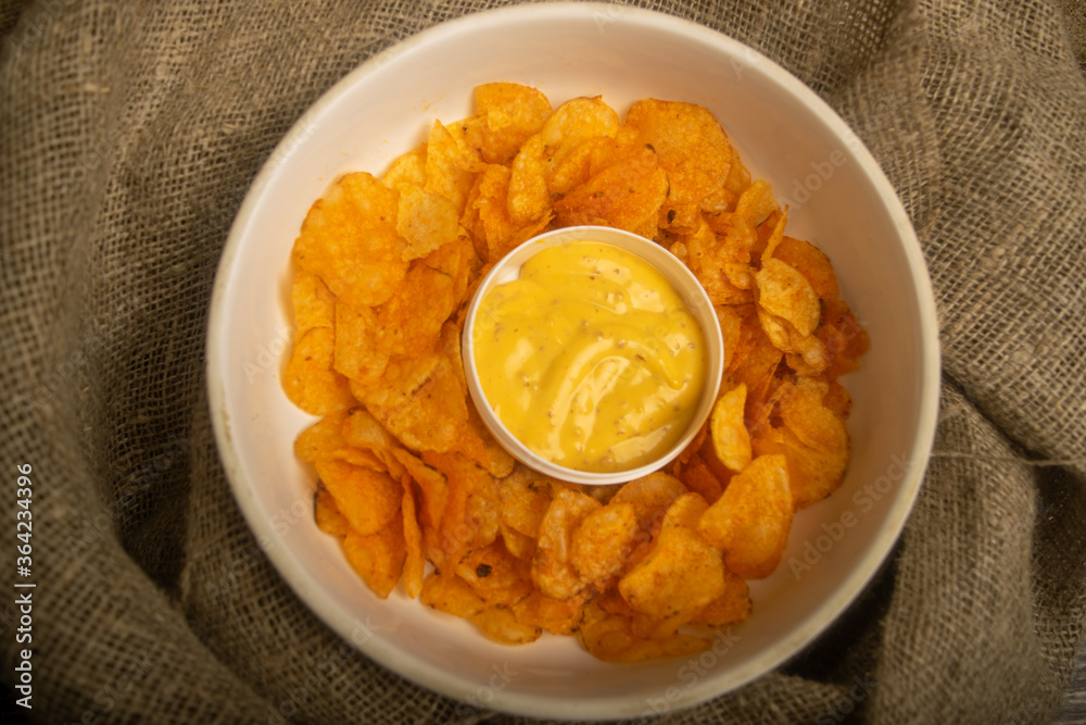 Potato chips on a round platter and a saucepan with cheese sauce. Close up. Potato chips on a round platter and a saucepan with cheese sauce. Close up.