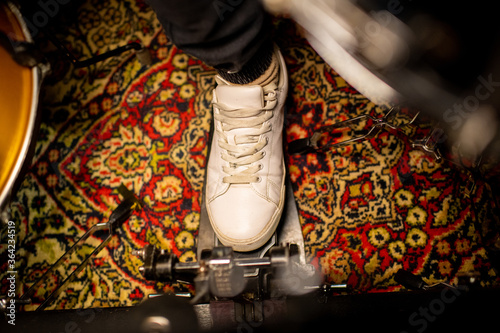 Foot of young musician wearing cross-shoes pushing pedal of electric drumset