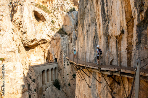 El Chorro, Spain. El Caminito del Rey walkway along the steep walls of a narrow gorge, narrow wooden platforms attached to vertical rocks over the precipice,  tourists walking.