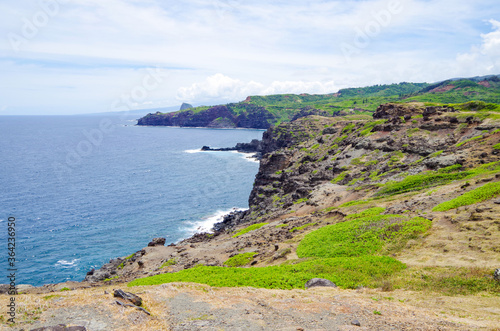 Panoramic view of rocky coastal line and shore of Kapalua Coast on Northern Maui peninsula with lush vegetation and sharp lava rocks and massive hills and mountains photo