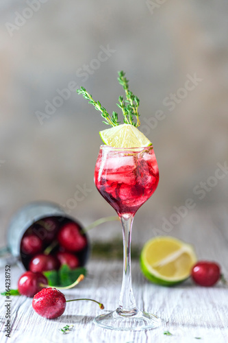 Cherry red cocktail with lime. Fresh summer cocktail with cherries, thyme and ice cubes.