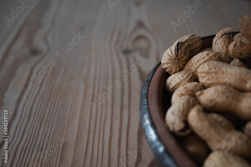 Close up shot of a bowl of raw peanuts or monkey nuts off to the lower right side of the frame. Set against a natural wood table or background with space for copy text