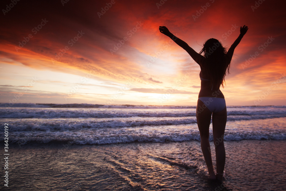 Woman in bikini by sea at sunset