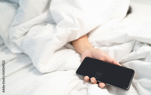 Woman lying on the bed and holding smartphone in hand, Social Addict Concept. Woman sleeping in bed being woken by mobile phone 