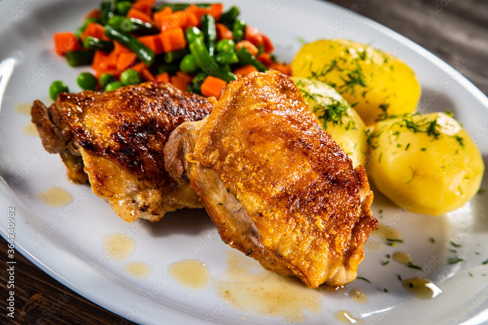 Roasted chicken thighs with boiled carrots, peas and potatoes on wooden background Roasted chicken thighs with boiled carrots, peas and potatoes on wooden background