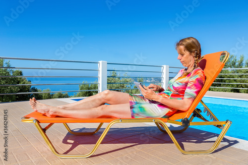 European woman on lounger reading tablet photo