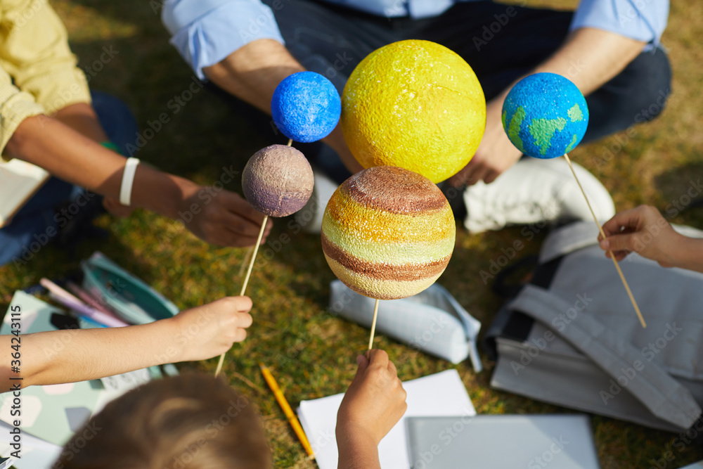 Close up of group of children holding model planets while enjoying outdoor astronomy class in sunlight, copy space - obrazy, fototapety, plakaty 