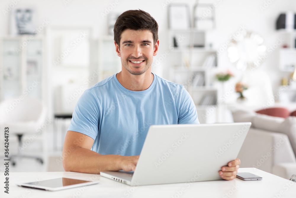 Portrait of smiling young man sitting at his desk with laptop, electronic tablet and mobile phone. Freelancer. Portrait of smiling young man sitting at his desk with laptop, electronic tablet and mobile phone. Freelancer.