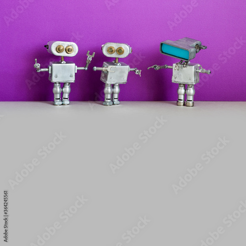Simplified design robotic toys. Three metal silver robots on purple gray background. Two of the same type and one special with a head monitor computer and copy space on blue interface.
