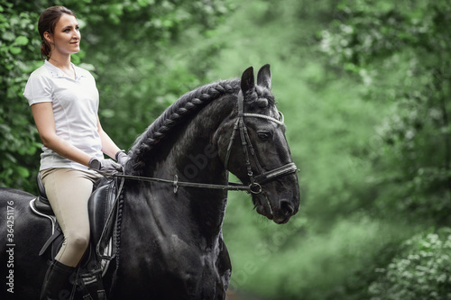 closeup portrait of young woman rides black friesian stallion in forest