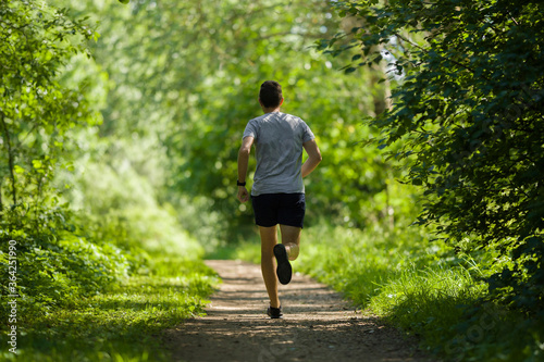Foto One young, adult man running in forest on natural trail in sunny summer day