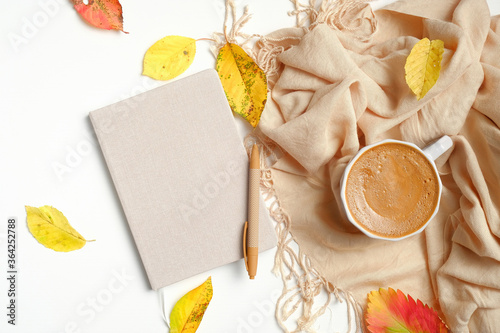 Flat lay paper notebook, pen, hot coffee cup, beige scarf, fallen leaves on white background. Top view autumn composition, cozy feminine workspace. photo