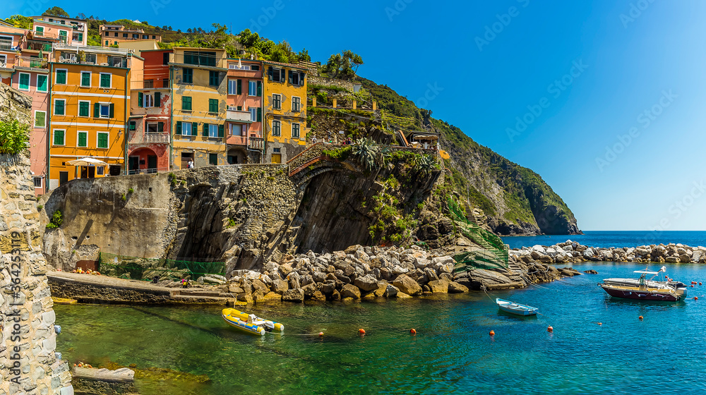 Colourful houses in the Cinque Terre village of Riomaggiore, Italy overlook the crystal clear waters of the harbour in the summertime
