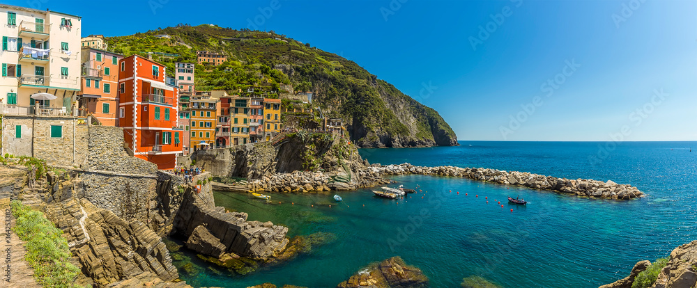 A panorama view of colourful houses and crystal clear waters in the Cinque Terre village of Riomaggiore, Italy in the summertime